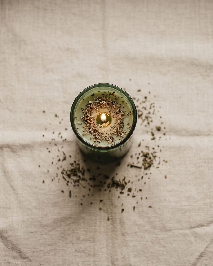 A lit green vigil candle dressed with herbs.