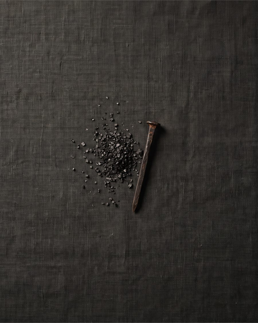 An iron nail and a scatter of black salt on dark linen.