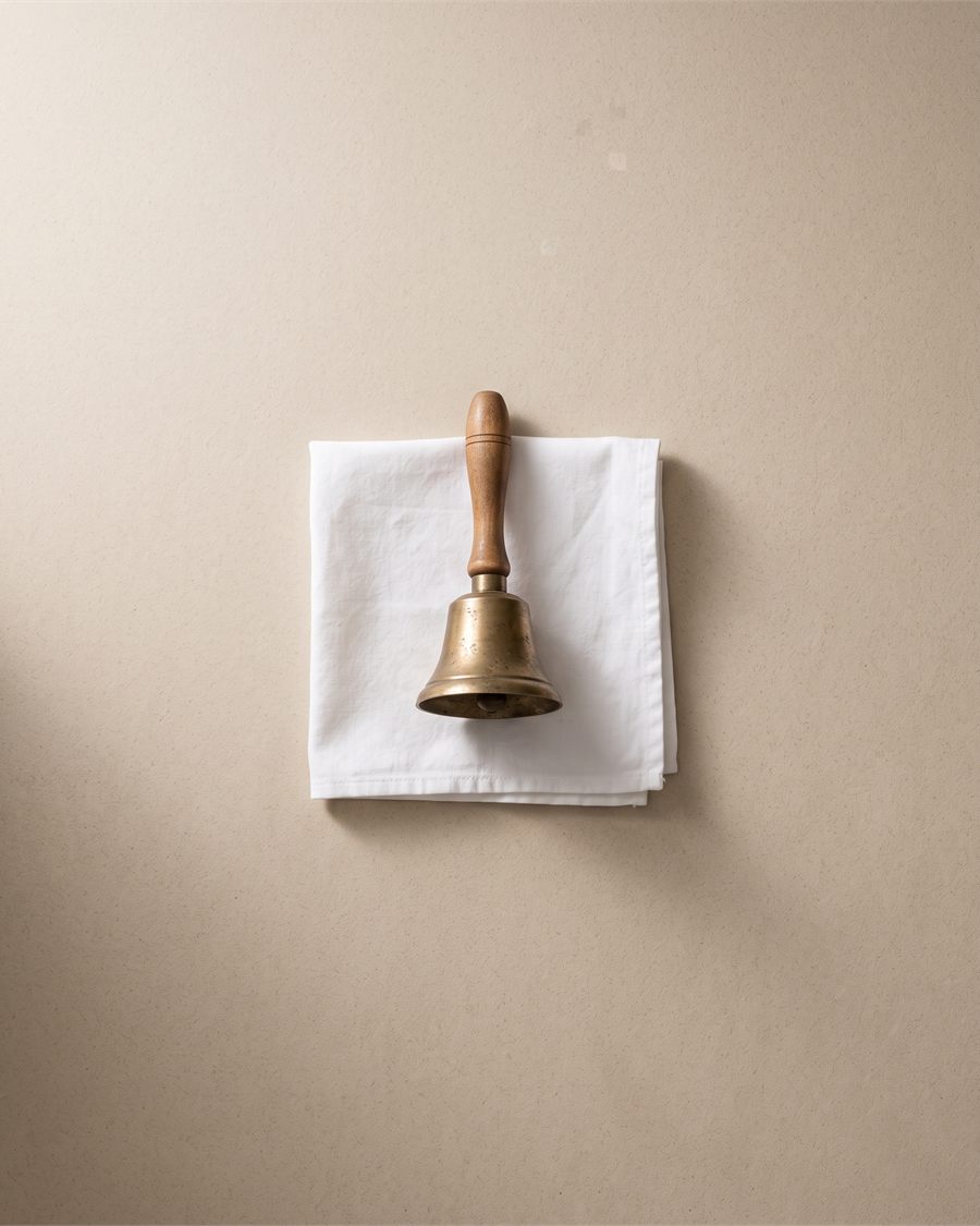 A small brass bell on white cloth in soft light.